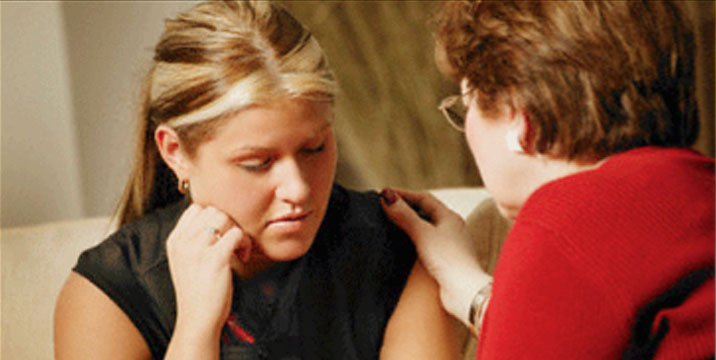 Two women seeking mental health care support each other during a conversation on a couch.