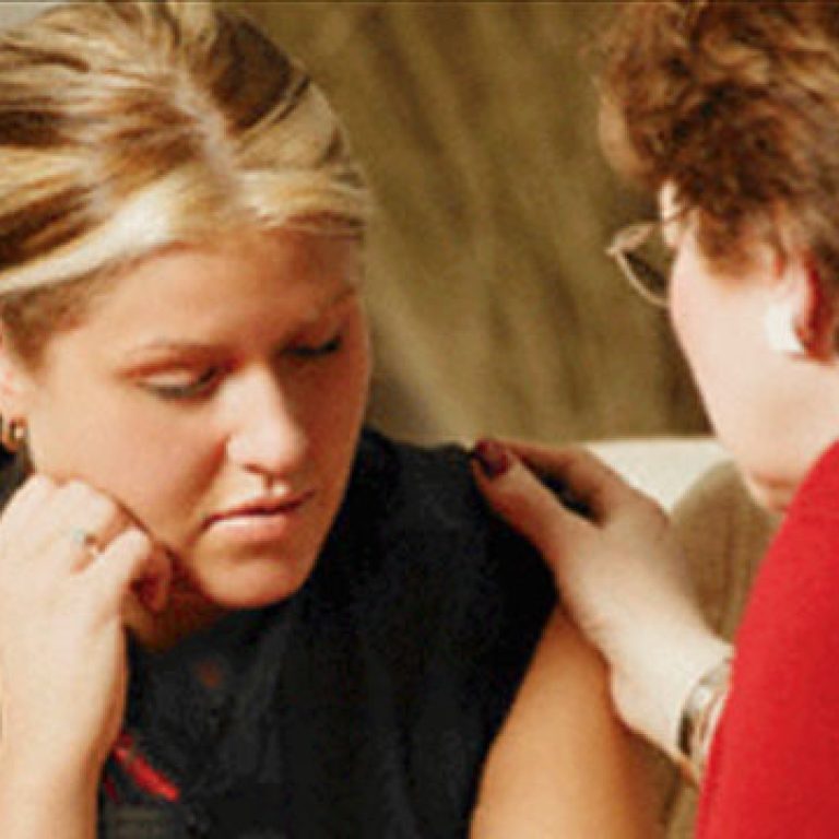 Two women seeking mental health care support each other during a conversation on a couch.